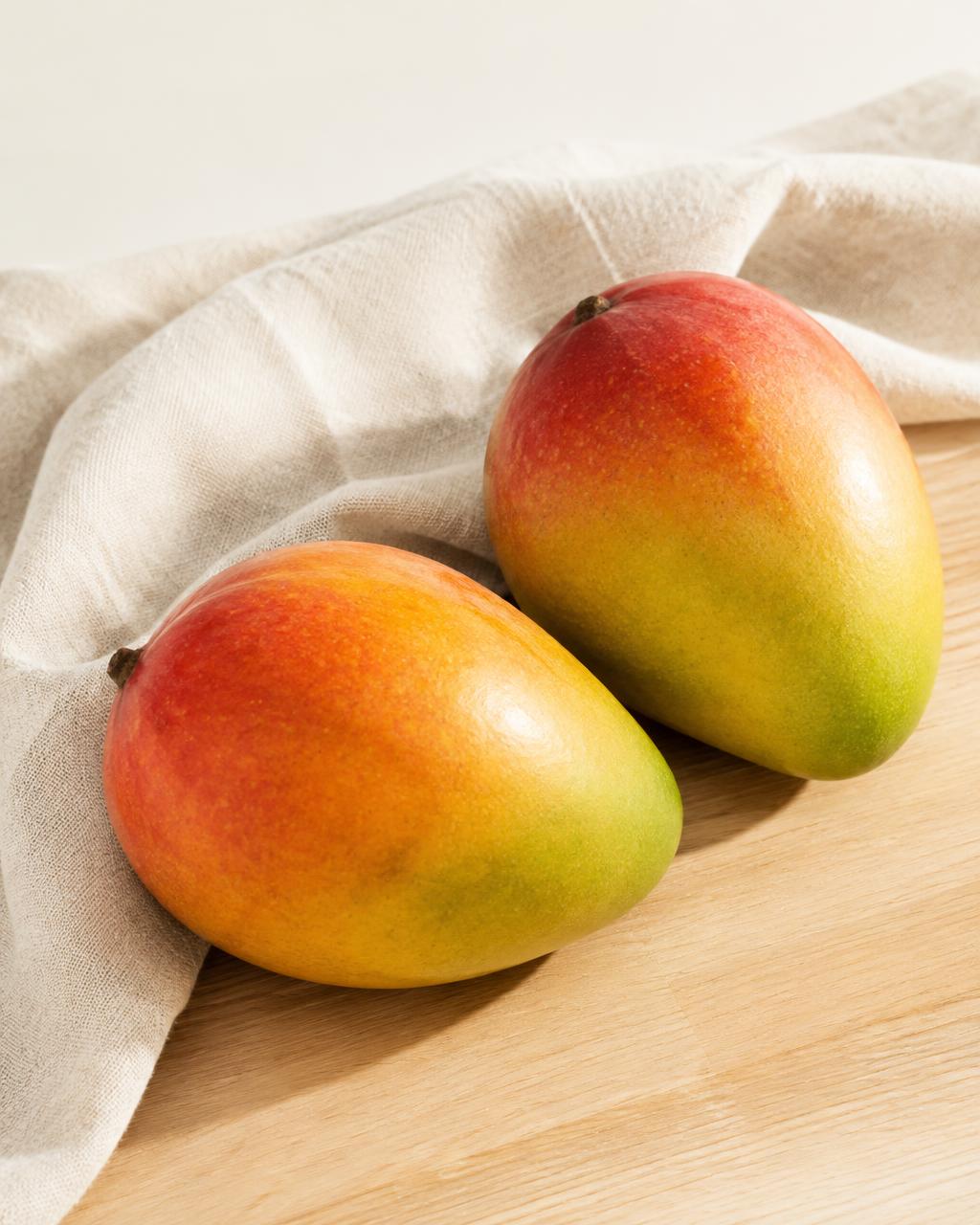 Dos mangos frescos sobre una tabla de madera con un lienzo de lino